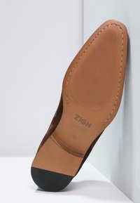 Scarpa in suede marrone con suola in pelle color nocciola, dotata di una finitura testurizzata, tacco in gomma nera e logo del brand impresso sulla suola.