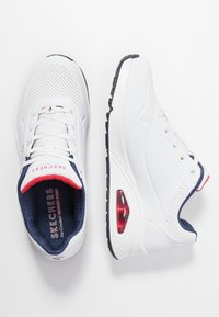 Bílé atletické boty s perforovaným designem, námořnickými akcenty a červenými detaily. Disponují silnou bílou podrážkou s viditelným vzduchovým polstrováním.