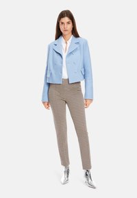 Hellblaues, tailliertes, doppelt knöpfbares Jacket, weißes Hemd, karierten braune Hose und glänzende silberne Knöchelstiefel. Glatte Stofftexturen.