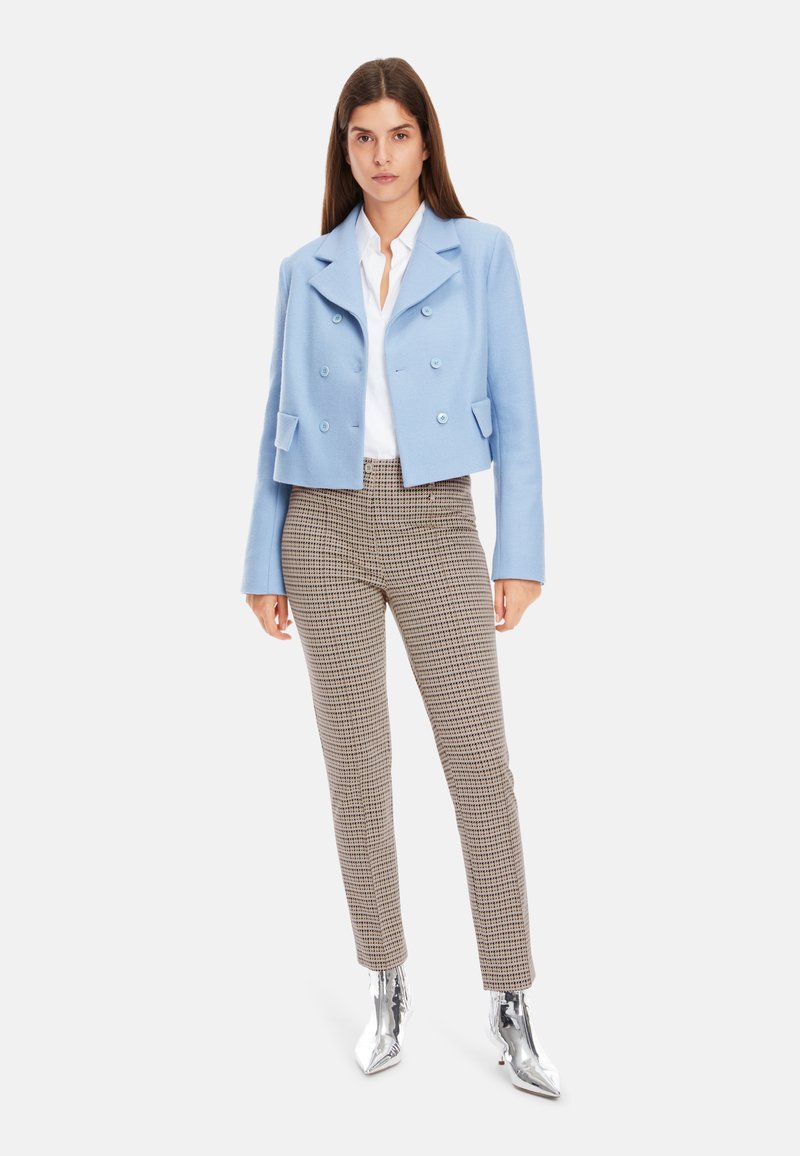 Hellblaues, tailliertes, doppelt knöpfbares Jacket, weißes Hemd, karierten braune Hose und glänzende silberne Knöchelstiefel. Glatte Stofftexturen.