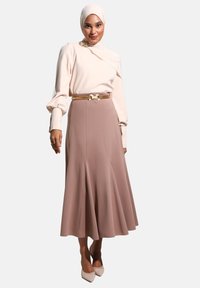 Haut beige à manches longues avec un design drapé et des manches bouffantes, associé à une jupe évasée rose poudrée de longueur cuisse et une ceinture avec accents dorés.