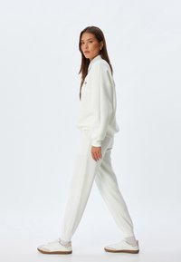 Weißer Pullover und passende Hose aus weichem Stoff. Das Design zeichnet sich durch einen lockeren Schnitt mit gerippten Bündchen und seitlichen Taschen aus.