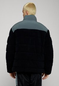 Dunjakke med mørk marineblå farge, horisontalt vattert design og en lys grå øvre del. Mykt, strukturert stoff med høy krage.