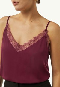Burgundy camisole with delicate lace trim along the V-neckline and adjustable spaghetti straps. Smooth fabric and relaxed fit.