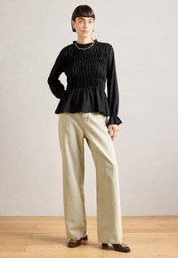 Top nero a maniche lunghe con corpino arricciato e orlo a peplum, abbinato a pantaloni a gamba larga di colore chiaro e scarpe con tacco quadrato bordeaux.
