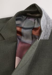 Blazer gris foncé avec doublure intérieure soyeuse multicolore et col en laine gris clair contrastant, posé à plat sur un fond neutre.
