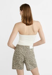Haut ajusté beige clair et short taille haute avec un motif léopard, présentant une texture subtile et une étiquette au dos du short.