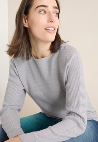 Jasnoszary sweter prążkowany z długimi rękawami, okrągłym dekoltem i teksturowanym materiałem. Połączony z tealowymi dżinsami dla uzyskania kontrastu.