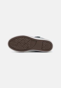 Suela de goma marrón con un patrón de agarre texturizado, entresuela blanca y un acabado liso. Presenta un pequeño logo embosado en la suela.