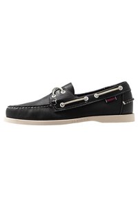 Zapato náutico de cuero negro con costuras blancas, cierre de cuerda y suela de goma de color claro en contraste, que presenta una etiqueta de logo en el lateral.