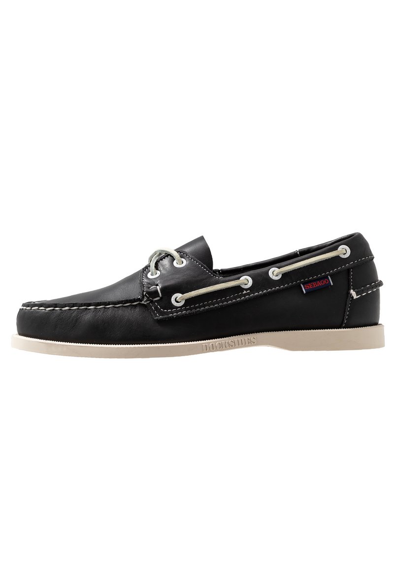 Zapato náutico de cuero negro con costuras blancas, cierre de cuerda y suela de goma de color claro en contraste, que presenta una etiqueta de logo en el lateral.