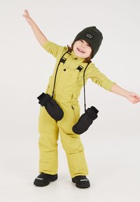 Geel sneeuwpak met verstelbare banden, zwarte handschoenen die aan de banden hangen, groene muts en zwarte laarzen. De stof lijkt waterdicht en geïsoleerd te zijn.