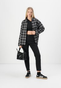 Svart og grå rutete skjorte over en svart crop top, parret med høy-levd svarte jeans og svarte sneakers med hvite striper. Strukturerte svarte veske.