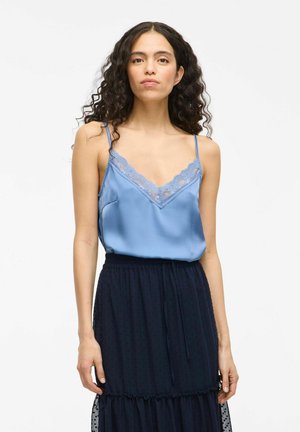 Light blue satin camisole with lace trim, paired with a navy tiered skirt featuring polka dot texture and an elastic waistband.