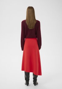 Bordeauxroter Strickpullover, roter midilanger Rock, schwarze kniehohe Stiefel. Weiche Textur, figurbetonte Silhouette und elegantes Design.