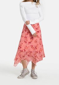 Blommig, rosa chiffongkjol med en hög-låg nederdel, lagerdesign och utspridda ros-mönster, tillsammans med grå hög-topps sneakers.