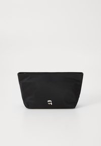 Čierna nylonová taška so zipsom na vrchu, mierne zužujúci sa dizajn; na prednej strane má minimalistický strieborný logový detail. Hladký povrch.