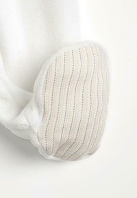 Tissu en peluche blanc au toucher doux, avec une zone d'accentuation présentant des rayures verticales beige et blanches ainsi que de petits points. Forme arrondie.