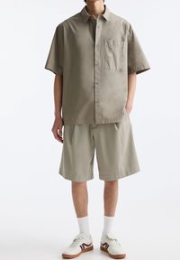 Lys beige kortærmet skjorte med en brystlomme, parret med matchende shorts til knæene. Båret med hvide sneakers og hvide sokker.