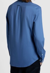 Camicia a maniche lunghe di colore azzurro chiaro realizzata in un tessuto morbido, con colletto button-down e dettaglio plissettato sul retro.