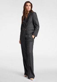 Traje gris a rayas con un blazer de doble botonadura y botones dorados, acompañado de pantalones ajustados. Tela suave con un corte estructurado.