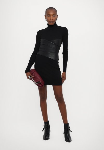 Robe noire ajustée avec des manches longues, accent en cuir à la taille, associée à des bottines noires et une pochette bourgogne.