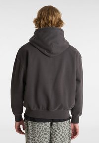 Grauer Hoodie mit hohem Kragen, lockerer Passform und gerippten Bündchen, kombiniert mit gemusterten, hellgrauen Shorts, die ein kariertes und Leopardenmuster aufweisen.