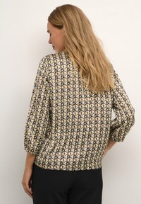 Long-sleeve blouse featuring a geometric pattern of gold and black, with a loose fit and gathered cuffs. Soft fabric with a smooth texture.
