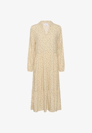 Beżowa sukienka z dekoltem w kształcie litery V, długimi rękawami i wielowarstwową spódnicą. Całość ozdobiona wzorem rozrzuconych czarnych kropek. Lekka tkanina.