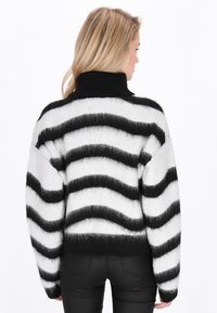 Zwart-wit gestreepte sweater met hoge hals, pluizige textuur, brede mouwen en een cropped pasvorm, met golvende lijntjespatronen.