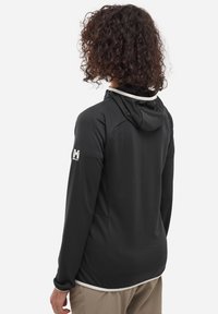 Schwarze Kapuzenjacke aus strukturiertem Stoff, mit weißem Saum am Kragen und einem Logo auf dem linken Ärmel. Verfügt über seitliche Taschen.