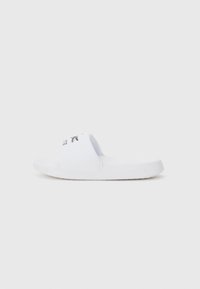 Vit slidesandal gjord av syntetiskt material, med ett brett rem med svart logotyp och en strukturerad sula för bra grepp.