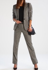 Grårutigt tvådelat kostym med en skräddarsydd kavaj med snedskurna slag och slim-fit byxor. Bärs med en svart topp och handväska.