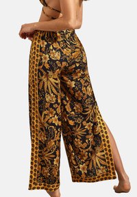 Pantalons larges noirs avec des motifs floraux dorés et jaunes, taille élastique et fentes latérales pour faciliter les mouvements et le style.