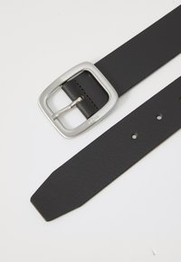 Fekete bőr öv négyzet alakú ezüst fém csattal. Sima textúra, hegyes véggel, több lyukkal a méretállításhoz. Minimalista design.