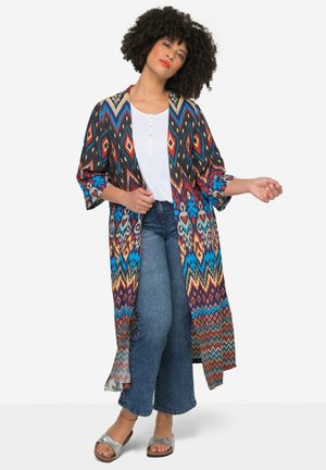 Long, lightweight kimono in multicolored geometric print. Features a patterned border with open sleeves, worn over a white top and denim.