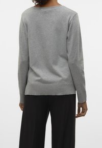 Šedý svetr s dlouhými rukávy, kulatým výstřihem a žebrovaným lemem. Měkká textura a volný střih. Nosený s volnými černými kalhotami, pohled zezadu.