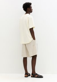 Light beige short-sleeve t-shirt, loose fit. Linen blend shorts in light tan with side pocket. Black strappy sandals.