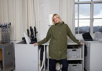 Alyvuogių žalios spalvos neperšlampama parka su gobtuvu, su spaudėtais mygtukais, šoninėmis kišenėmis ir raišteliais, nufotografuota studijoje su įranga.