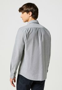 Camisa gris de manga larga con botones, hecha de una tela ligera, que cuenta con un collar en punta, puños con botones y un detalle de pliegues en la espalda.
