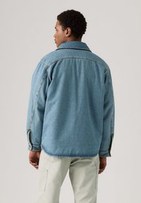 Chaqueta de mezclilla en azul claro con un corte relajado, gran cuello y bolsillos laterales. Presenta costuras visibles y un dobladillo redondeado.