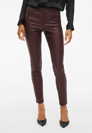 Pantalon en cuir bordeaux foncé ajusté, porté avec des escarpins noirs à bout pointu et une chemise noire à manches longues avec boutons.
