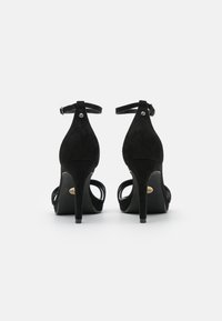 Melnas zamšādas augstpapēžu sandales ar plānām potīšu siksniņām, atvērtu purngalu un elegantu siluetu. Iespējas ar slaidu stiletto papēdi un metalizētām akcentiem.