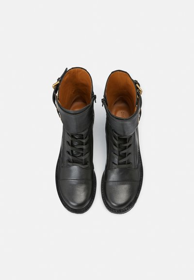 Black leather ankle boots with a rounded toe, lace-up design, and gold hardware accents. Interior is brown with a smooth texture.