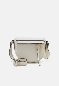 Bolso cruzado redondo de color gris claro con tapa magnética, ribete negro, herrajes dorados y una correa removible. Presenta un detalle en forma de anillo circular.