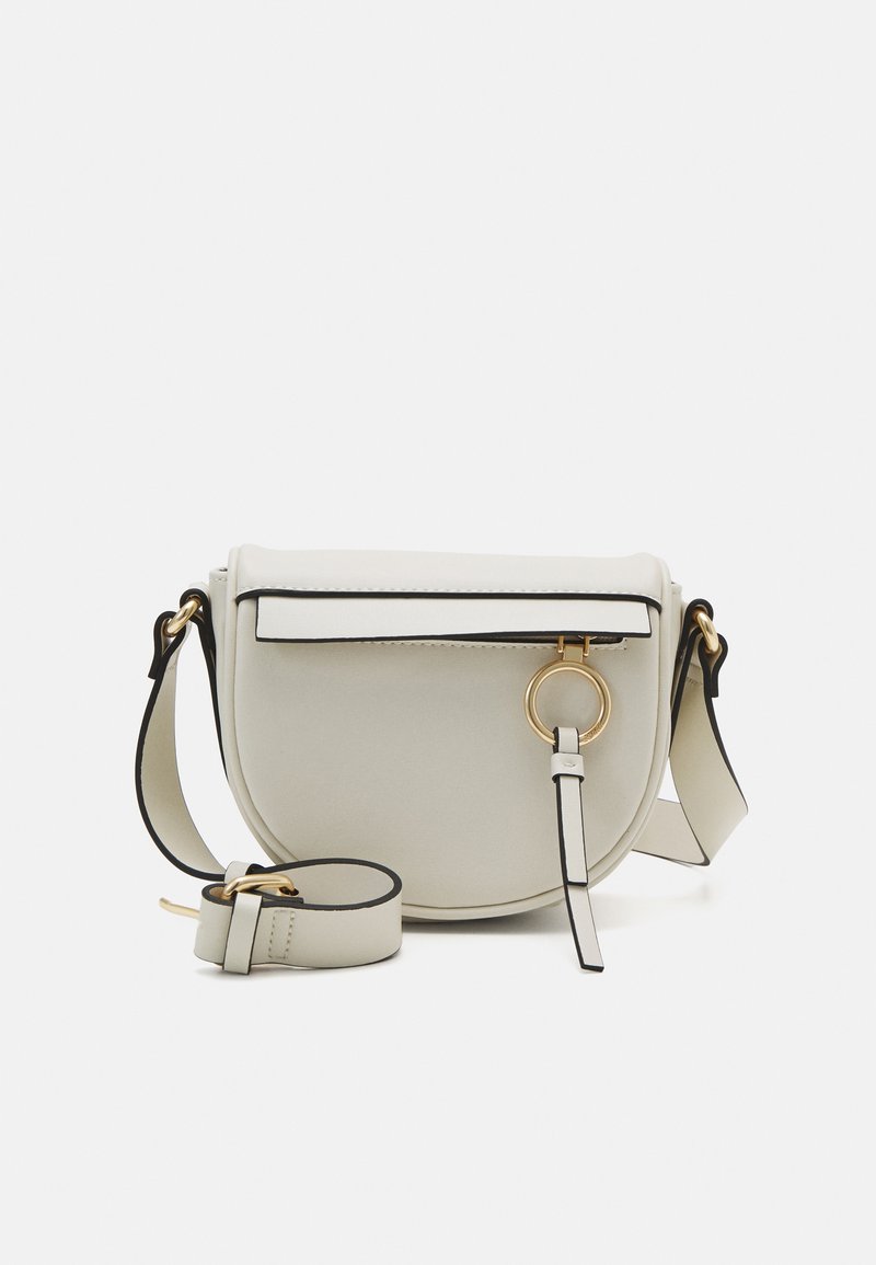 Bolso cruzado redondo de color gris claro con tapa magnética, ribete negro, herrajes dorados y una correa removible. Presenta un detalle en forma de anillo circular.