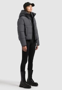 Pelēks pūkains jakas ar augstu apkakli, ar rāvējslēdzēju priekšpusē un divām kabatām. Valkāts ar melnām legiņām un melnām auklu kareivju zābakiem.