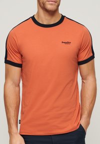 Orange kortærmet t-shirt med sorte detaljer ved halsudskæringen og ærmerne, med et lille sort SuperDry-logo på brystet. Glat tekstur.