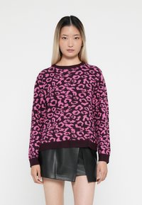 Maglione a maglia con una base viola scuro e stampa leopardata rosa brillante. Collo e polsini a costine. Abbinato a una gonna in pelle nera.