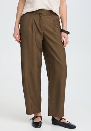 Femme portant un pantalon marron à jambes larges, des ballerines Mary Jane noires, un haut en maille blanc et un bracelet noir au poignet droit.